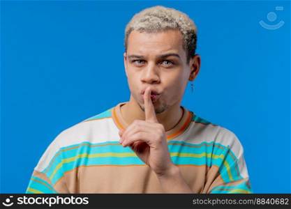 Handsome man with gesture of shhh, secret, silence, conspiracy, gossip concept. Smiling guy holding finger on lips, blue studio background. . High quality photo. Handsome man with gesture of shhh, secret, silence, conspiracy, gossip concept. Smiling guy holding finger on lips, blue studio background. 