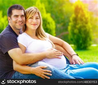 Handsome man with pregnant wife relaxing outdoors, happy parenthood, summer weekend, togetherness and support concept