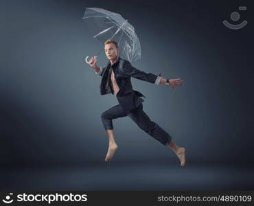 Handsome manager jumping with a transparent umbrella