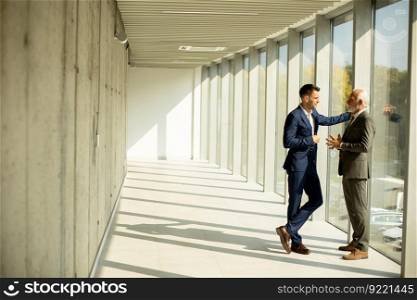 Handsome mature businessman and his young colleague discussing in the office corridor