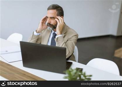 Handsome mature businessman in classic suit  having a headache while working in his office