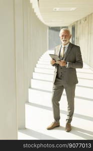 Handsome mature businessman standing with digital tablet in the office corridor