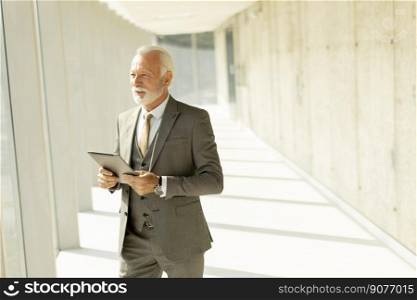 Handsome mature businessman standing with digital tablet in the office corridor