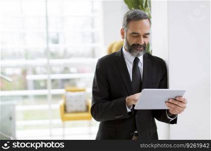 Handsome mature businessman with digital tablet in the office working, reading or searching something