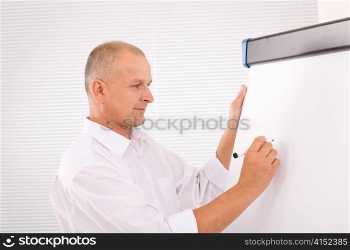 Handsome mature businessman writing at empty flip chart looking aside