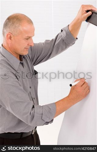 Handsome mature businessman writing at empty flip chart looking aside