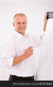 Handsome mature businessman writing at empty flip chart looking front