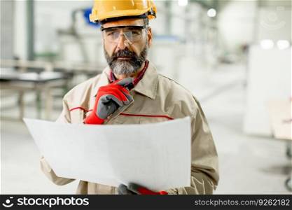 Handsome mature engineer looking at plan in the factory