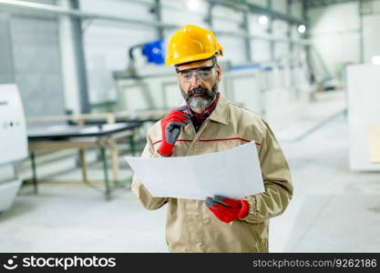 Handsome mature engineer looking at plan in the factory