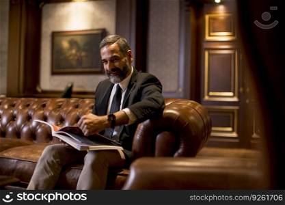 Handsome mature man in elegant suit reading a book in a luxurious apartment