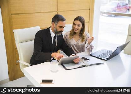 Handsome mature man with digital tablet and young woman business partners with laptop working in the office