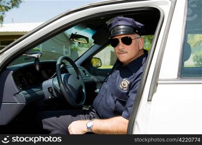 Handsome mature police officer on duty sitting in his squad car.
