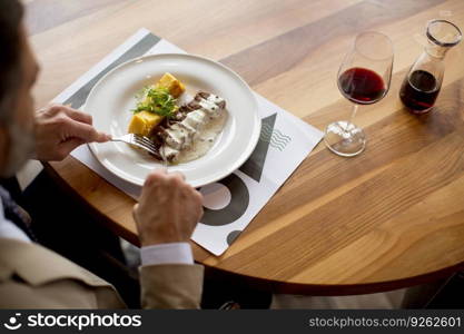Handsome middle aged businessman having lunch and drinking red wine in restaurant