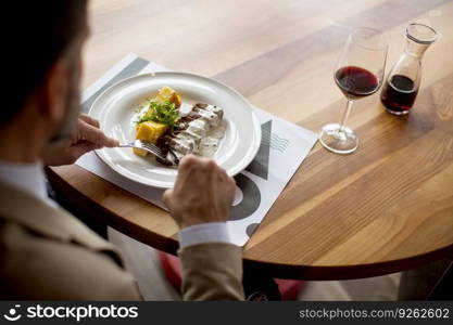 Handsome middle aged businessman having lunch and drinking red wine in restaurant