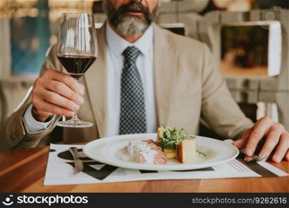 Handsome middle aged businessman having lunch and drinking red wine in restaurant