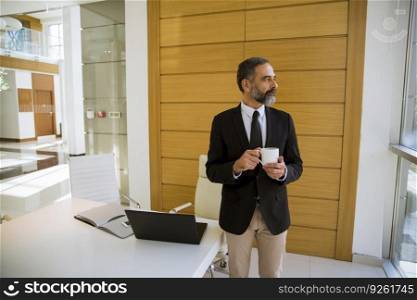 Handsome middle aged businessman holding cup of coffee or in the modern office