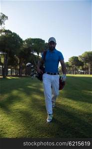 handsome middle eastern golf player carrying and bag and walking at course on beautiful morning sunrise