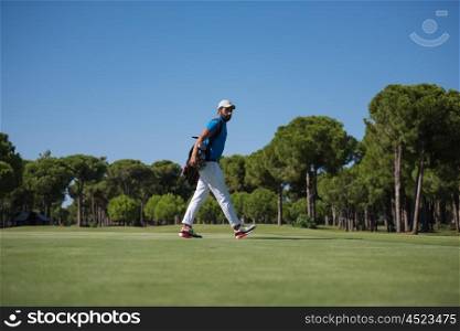 handsome middle eastern golf player carrying bag and walking at course to next hole