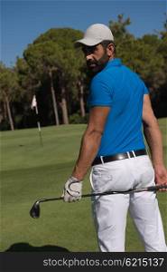 handsome middle eastern golf player portrait from back with course in background at beautiful sunny day