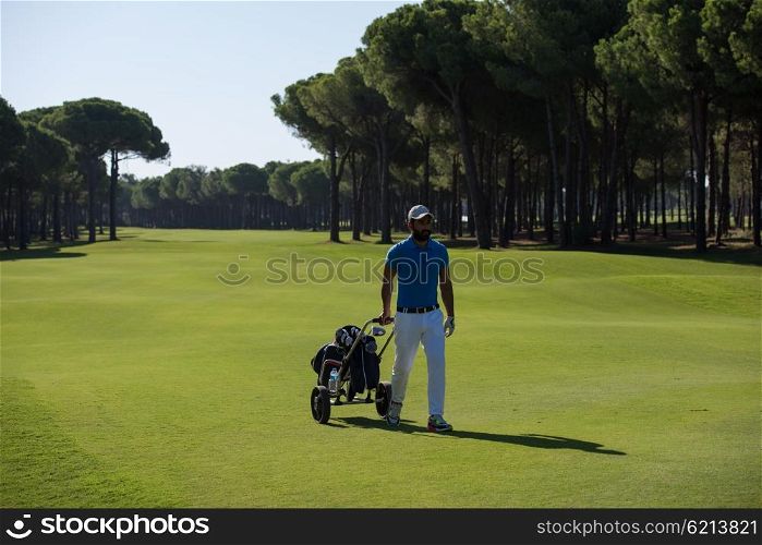 handsome middle eastern golf playerwalking with wheel bag at course on beautiful sunny day
