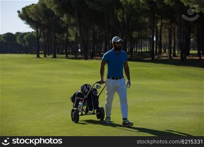 handsome middle eastern golf playerwalking with wheel bag at course on beautiful sunny day
