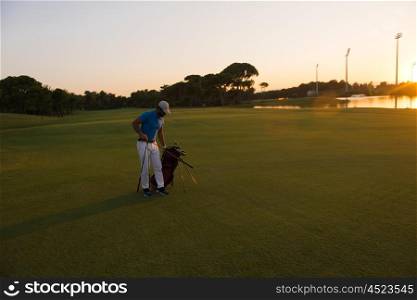 handsome middle eastern golfer carrying bag and walking to next hole at golf course on beautiful sunset in background