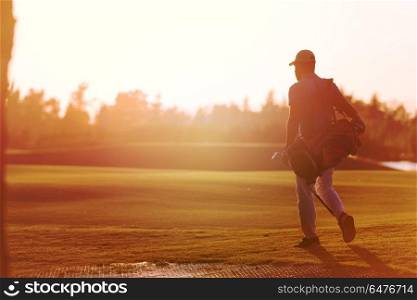handsome middle eastern golfer carrying bag and walking to next hole at golf course on beautiful sunset in background. golfer walking and carrying golf bag at beautiful sunset