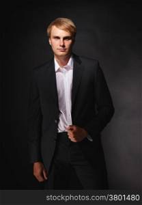 Handsome modern businessman wearing black suit, studio shot dark background
