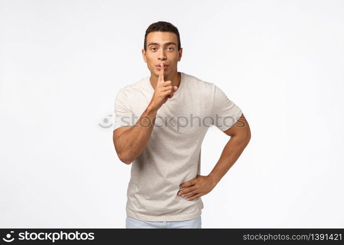 Handsome muscular boyfriend in casual t-shirt, prepare surprise for valentines day, shushing, making hush sound as press index finger to lips and smile, have secret, standing white background.. Handsome muscular boyfriend in casual t-shirt, prepare surprise for valentines day, shushing, making hush sound as press index finger to lips and smile, have secret, standing white background