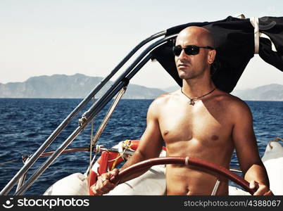 Handsome muscular man at the helm, sailing at Mediterranean sea, traveling the world by sailboat, male model on luxury yacht, water sport vacation, summer outdoors