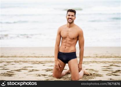 Handsome muscular man on his knees on the sand of the beach. Handsome man on his knees on the sand of the beach