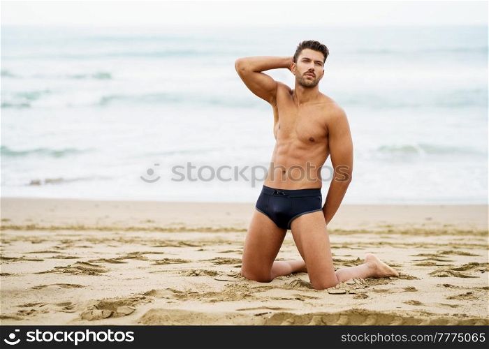 Handsome muscular man on his knees on the sand of the beach. Handsome man on his knees on the sand of the beach