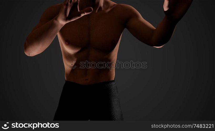 Handsome muscular shirtless young man standing in the dark
