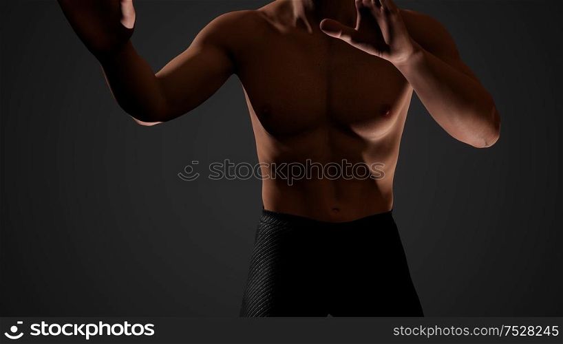 Handsome muscular shirtless young man standing in the dark
