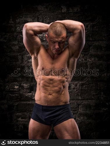 Handsome posing bodybuilder on a background of brick wall