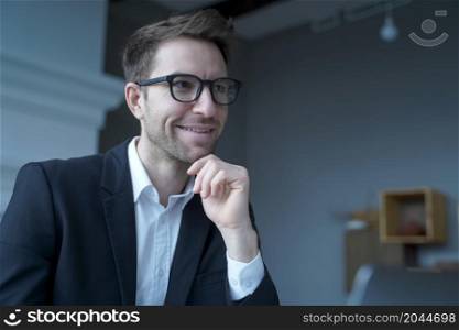 Handsome positive austrian businessman wearing glasses working remotely from home, enjoying freelance job on laptop computer, reading publications or internet news while sitting at office desk. Handsome positive austrian businessman wearing glasses working remotely from home