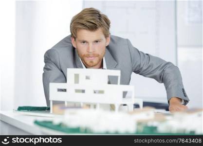 handsome real estate agent thinking next to scale model