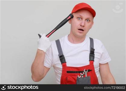 Handsome repairman wearing a helmet and an overall, holding a hammer in his hand, having fun, standing on a white background. Maintenance service. building concept. Handsome repairman wearing a helmet and an overall, holding a hammer in his hand, having fun, standing on a white background. Maintenance service. building concept.