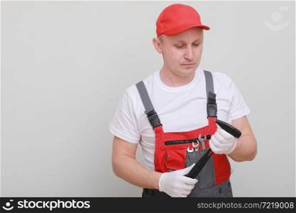 Handsome repairman wearing a red cap and an overall, holding a hammer in his hand, looking seriously, standing on a white background. Maintenance service. building concept. Handsome repairman wearing a red cap and an overall, holding a hammer in his hand, looking seriously, standing on a white background. Maintenance service. building concept.