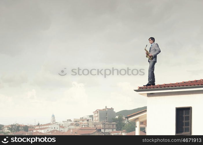 Handsome saxophonist. Young man in suit with saxophone in hands on house roof