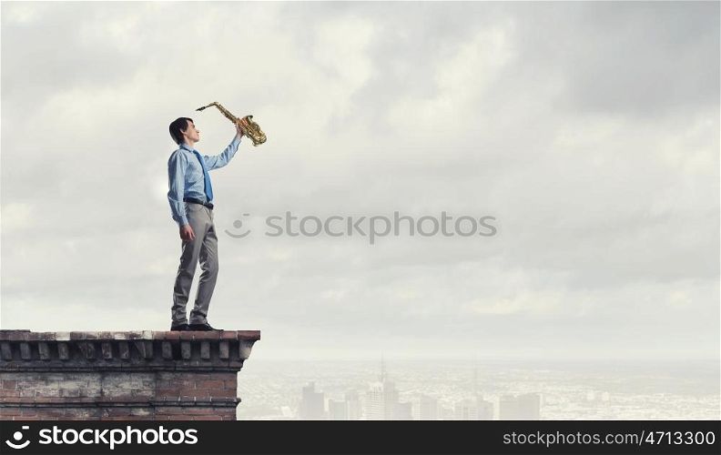 Handsome saxophonist. Young man in suit with saxophone in hands on house roof