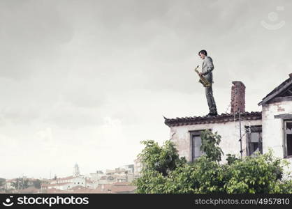 Handsome saxophonist. Young man in suit with saxophone in hands on house roof