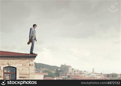 Handsome saxophonist. Young man in suit with saxophone in hands on house roof