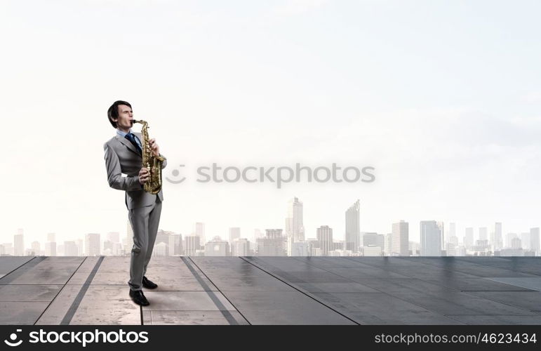 Handsome saxophonist. Young man on building roof playing saxophone