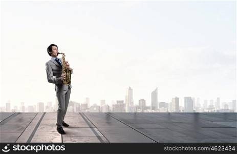 Handsome saxophonist. Young man on building roof playing saxophone