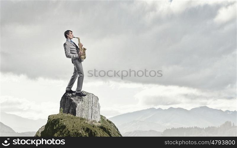 Handsome saxophonist. Young man on top of rock playing saxophone