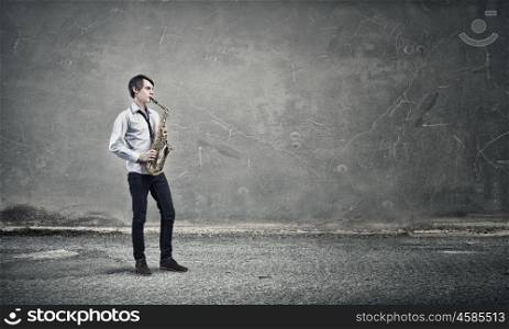 Handsome saxophonist. Young man playing saxophone in empty room