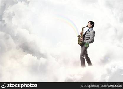 Handsome saxophonist. Young man playing saxophone on sky background