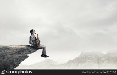 Handsome saxophonist. Young man sitting on rock edge playing saxophone