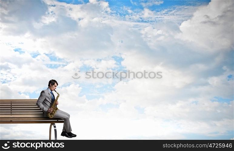 Handsome saxophonist. Young man sitting on wooden bench and playing saxophone